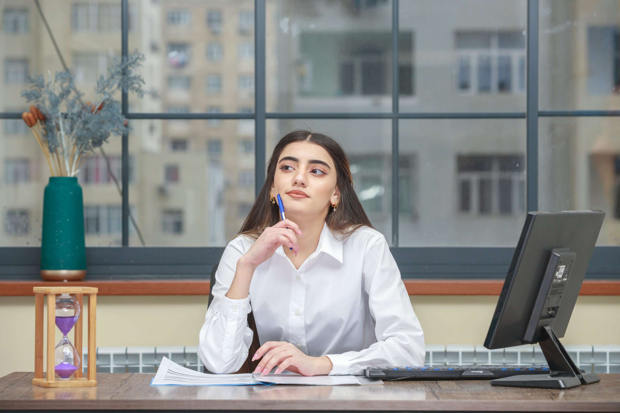 Portrait of a young businesswoman sitting at the desk and put her pen to her chin while thinking